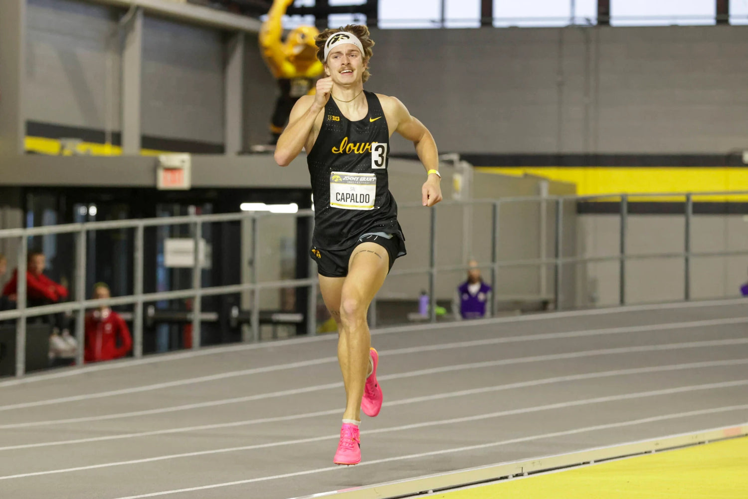 University of Iowa track athlete Sal Capaldo running indoors during a meet, wearing a black uniform and pink shoes